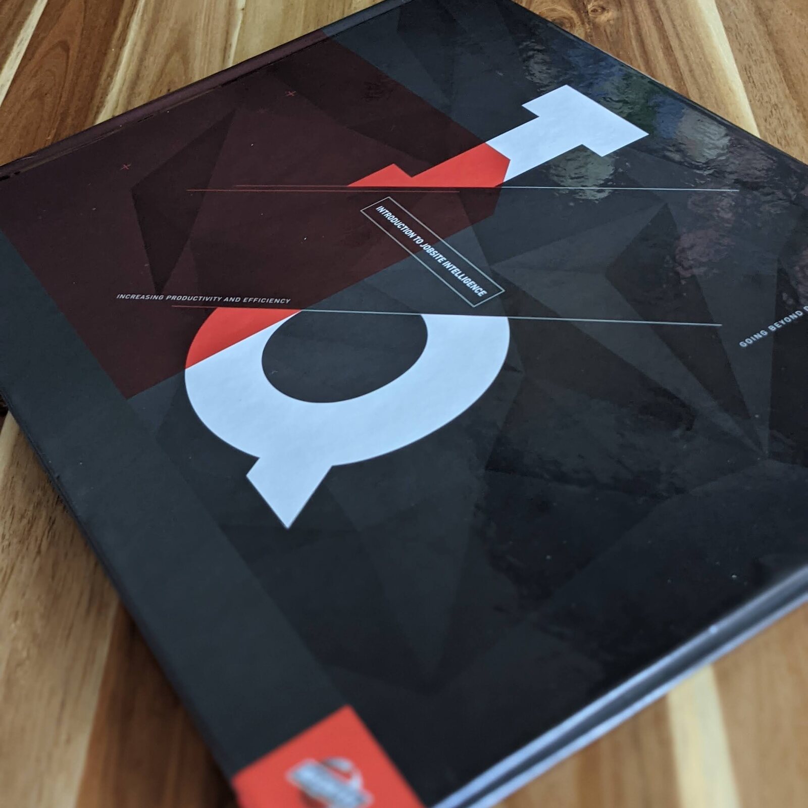 The printed Smart JobSite book on a wood table: a black cover with a large white and red mark, the line Increasing productivity and efficiency, and a red Bechtel tab at the corner.