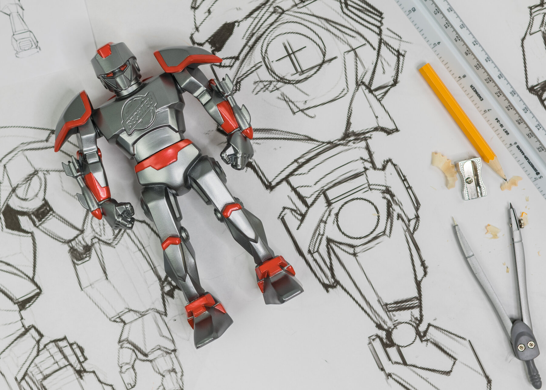 Overhead: the BechMech toy lying among rulers, pencils and robot sketches.